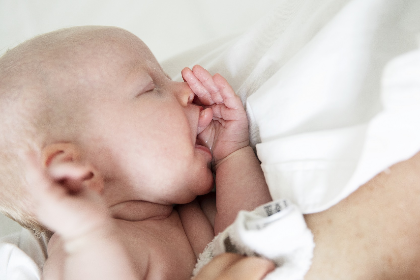 Ett två månaders spädbarn stoppar in sin hand i munnen som en tydlig amningssignal