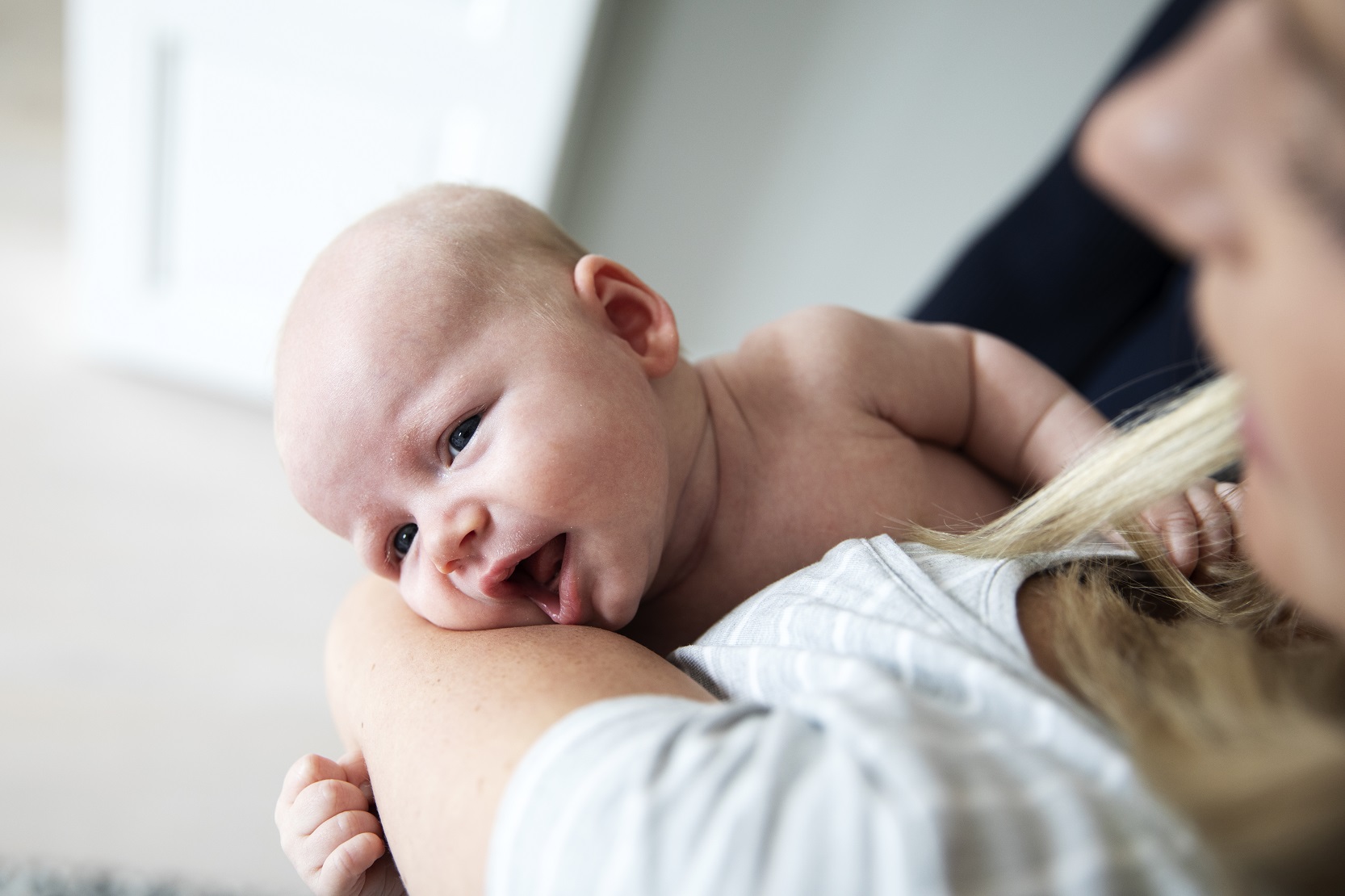 Ett två månaders spädbarn ligger på sin mammas arm och öppnar munnen som en tidig amningssignal