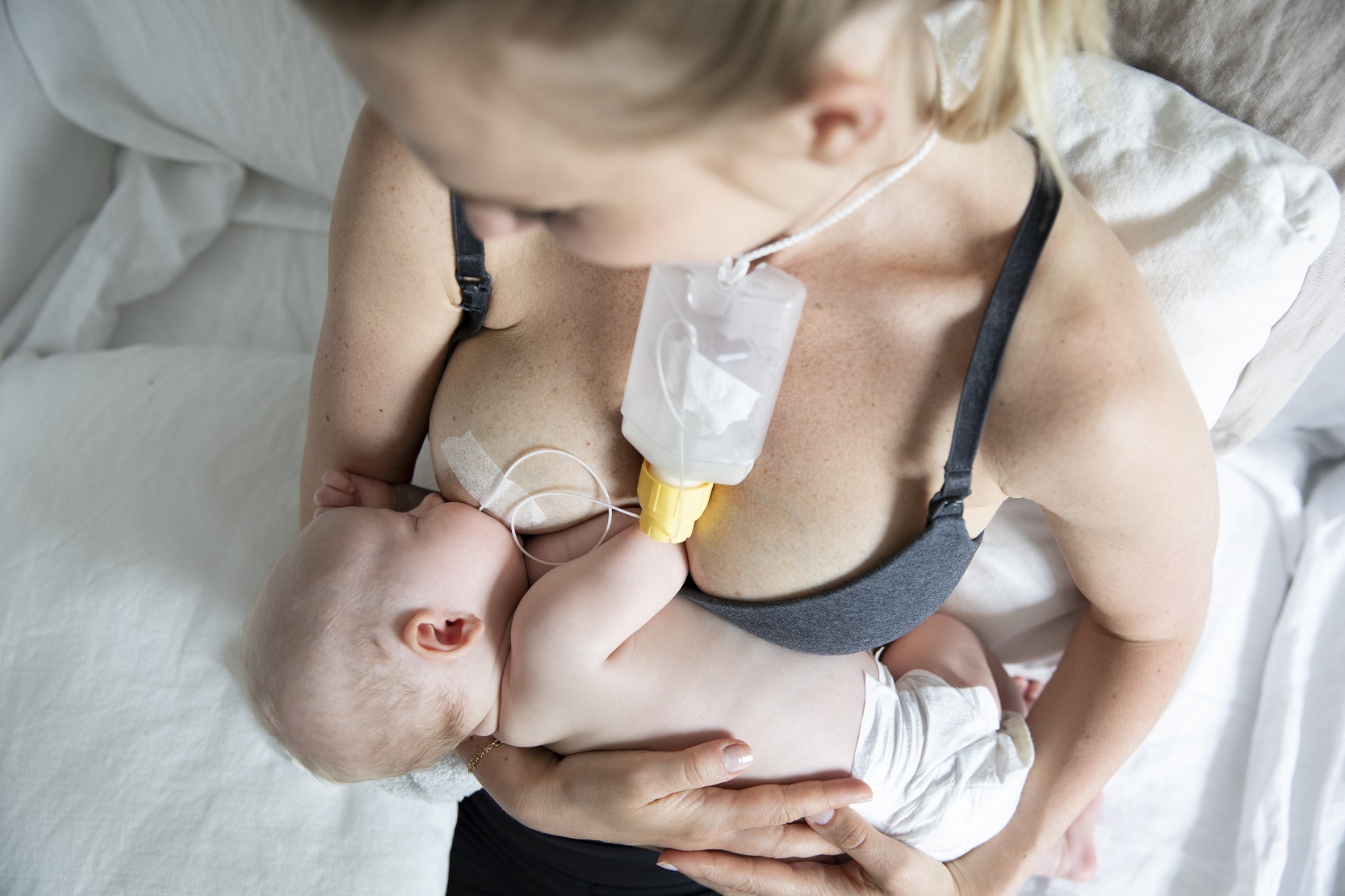 Mamma som håller en bebis som får bröstmjölk genom ett tillmatningsset som är fäst på bröstet.
