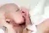 Ett barn som är en månad gammal ligger i sin mammas famn. Barnet lyfter ivrigt båda armarna i luften och suger på den ena handen.