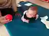 Ett spädbarn ligger på en filt på golvet och vrider huvudet för att titta på en räd boll som den vuxna håller i handen.