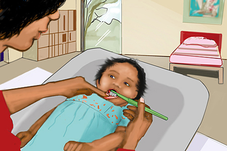 Vuxen person borstar tänderna på ett barn under ett år som ligger på ett skötbord.